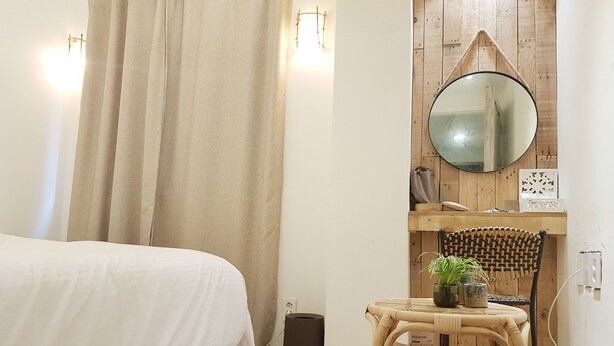 A bedroom with a bed, a small table with a plant, a chair, a round mirror, and a waste bin. - Hotel Elephant (Busan)
