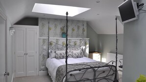 A bedroom with a four-poster bed, a skylight, a mounted TV, and a white wardrobe.