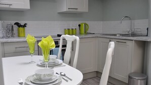 A modern kitchen with white cabinets, a stainless steel sink, and a dining table set with glassware and plates.