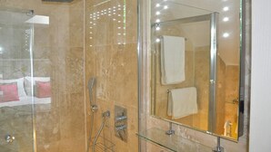 A modern bathroom with a glass-enclosed shower, a large mirror with lights, and a glass shelf.