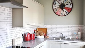 A kitchen with white cabinets, a large clock, and various kitchen items on the counter.