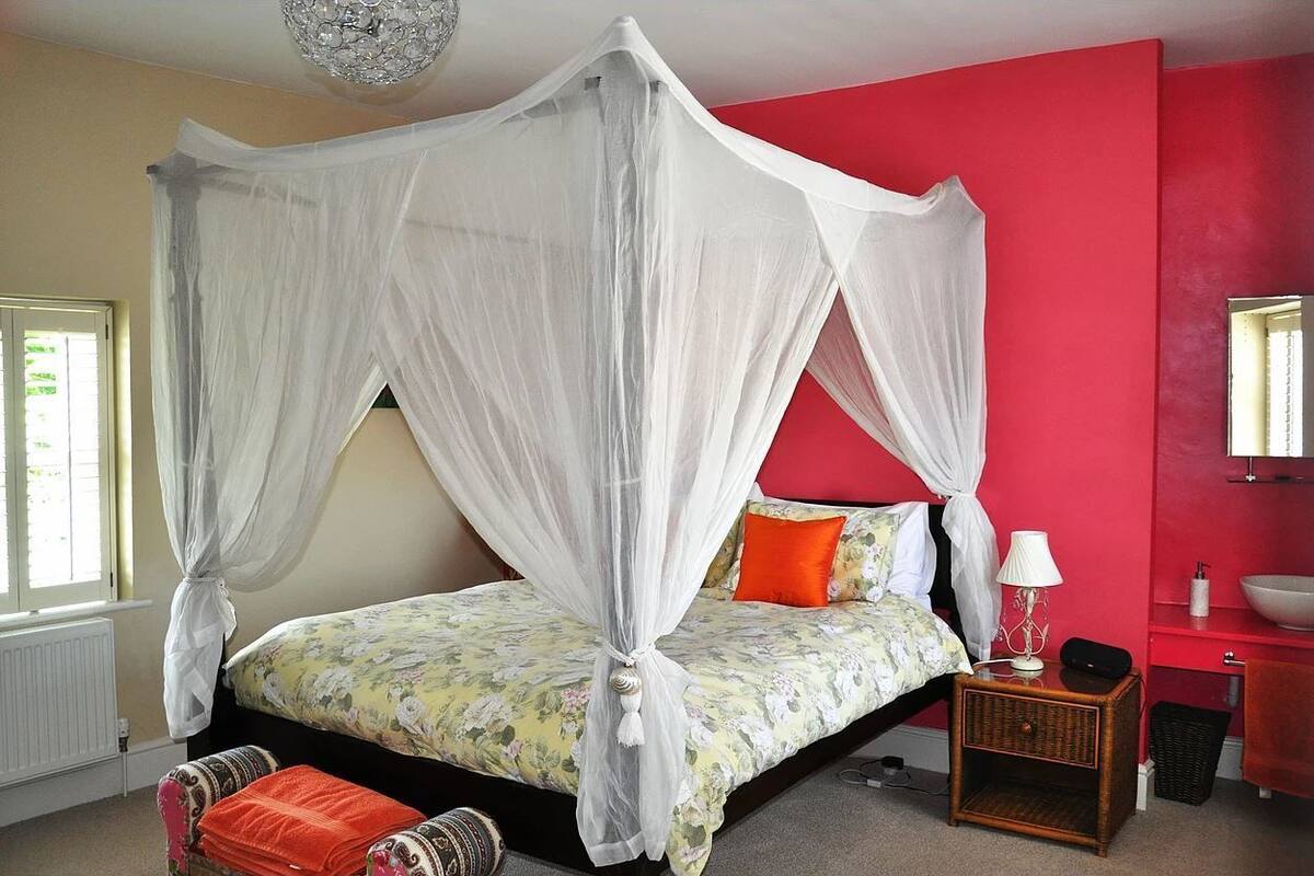 Une chambre à coucher avec un lit à baldaquin, une table de chevet avec une lampe et un mur d’accent rouge.