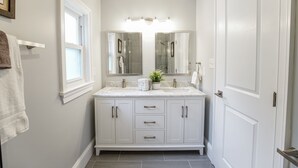 A bathroom with a double vanity, white cabinetry, a large mirror, and a window.