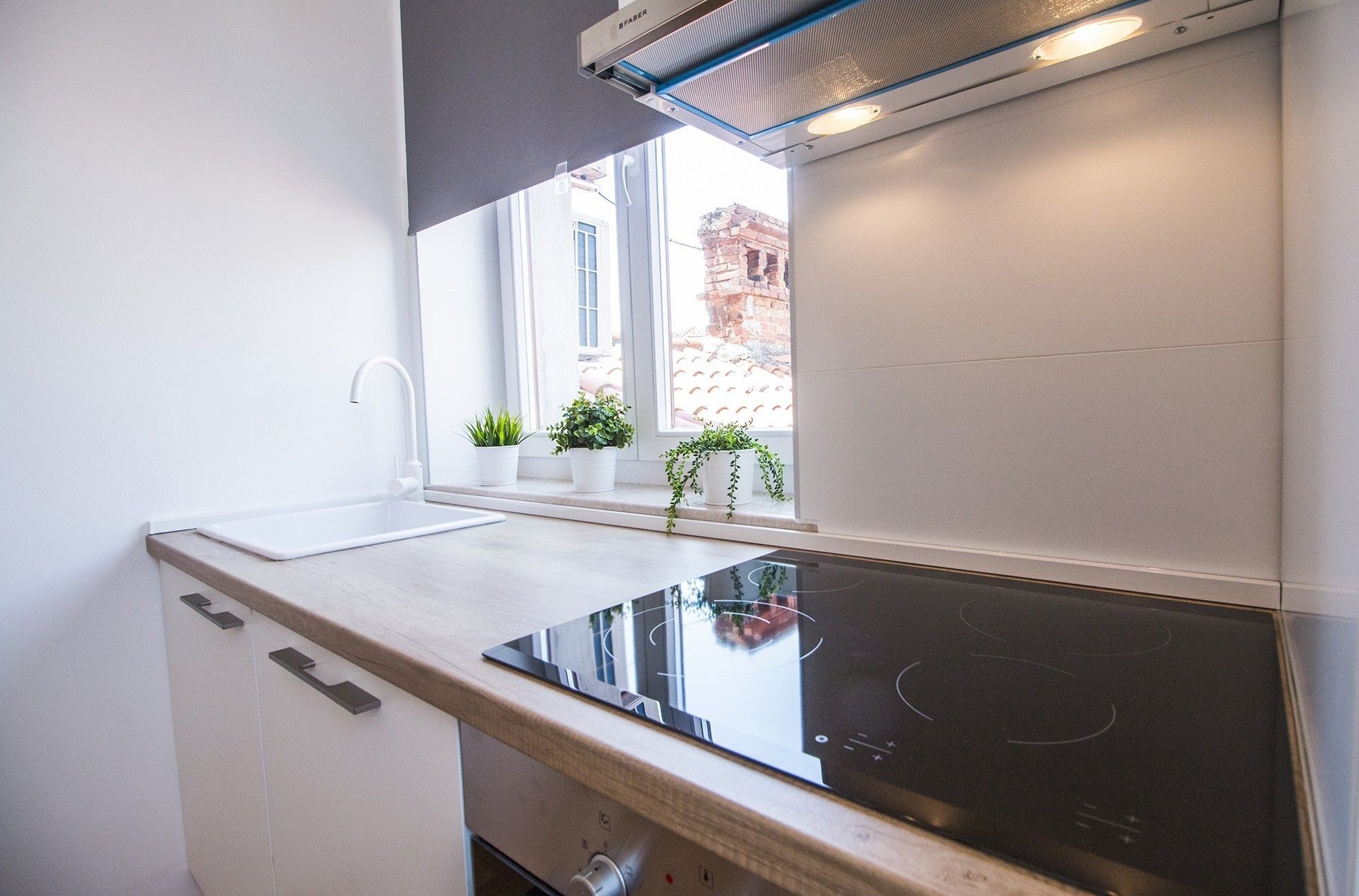 Une cuisine moderne dotée d’une cuisinière intégrée, d’une fenêtre ornée de plantes en pot et offrant une vue sur un bâtiment en briques à l’extérieur.