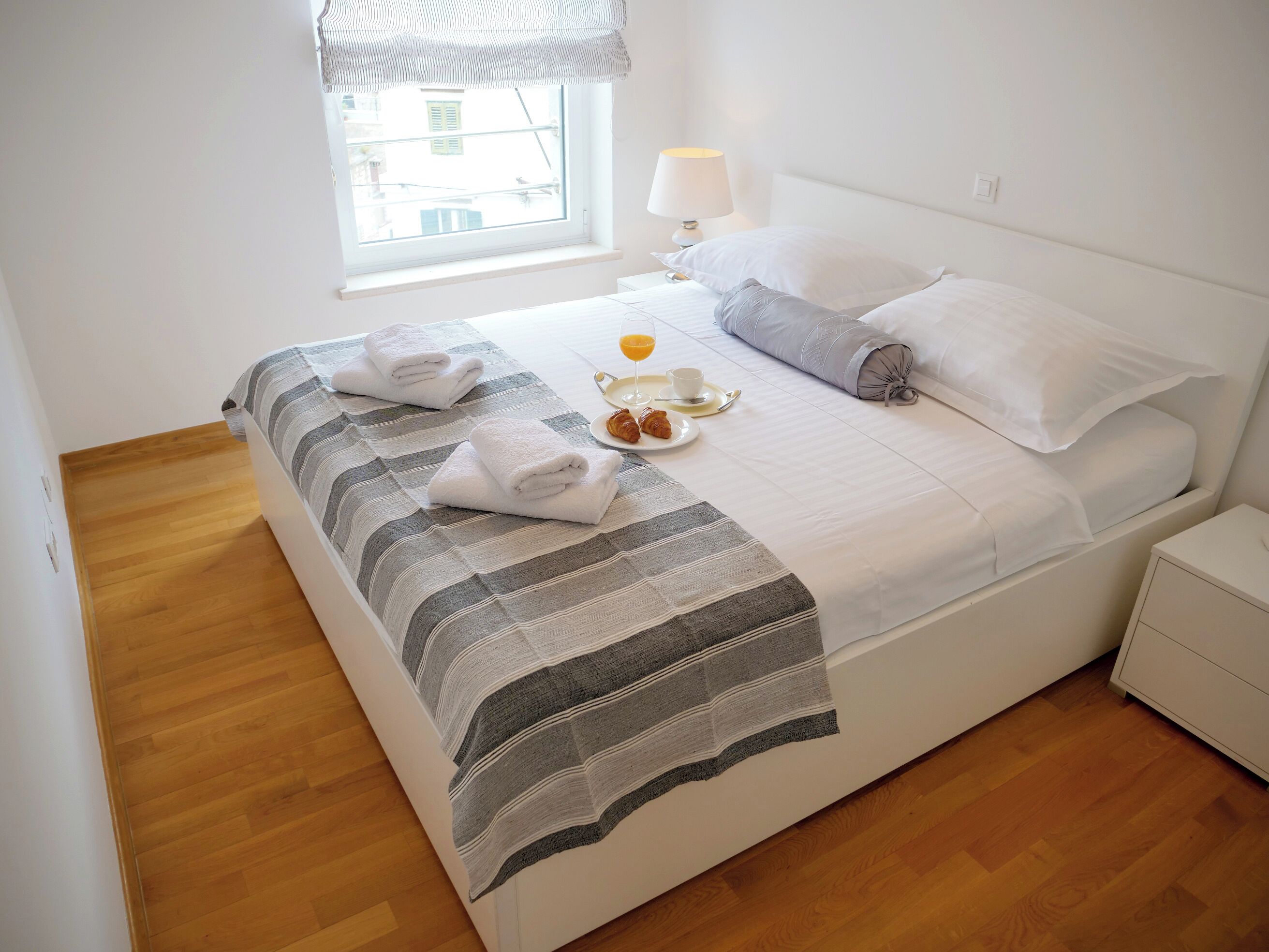 Uma cama bem arrumada com toalhas, uma mesa de cabeceira com abajur e um tabuleiro de café da manhã.