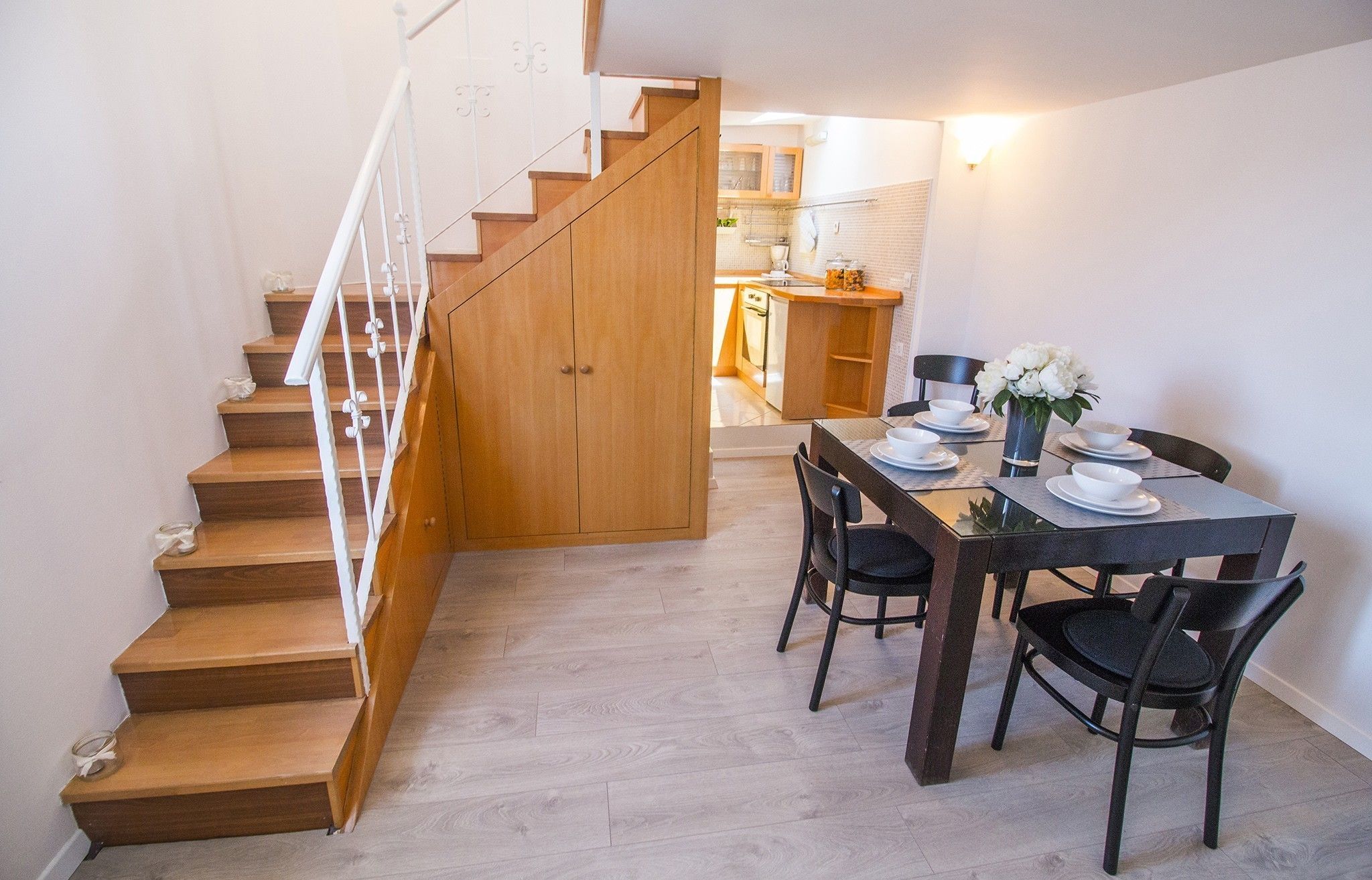 A dining area with a wooden staircase leading to a kitchen.