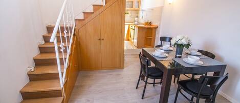 A dining area with a wooden staircase leading to a kitchen.