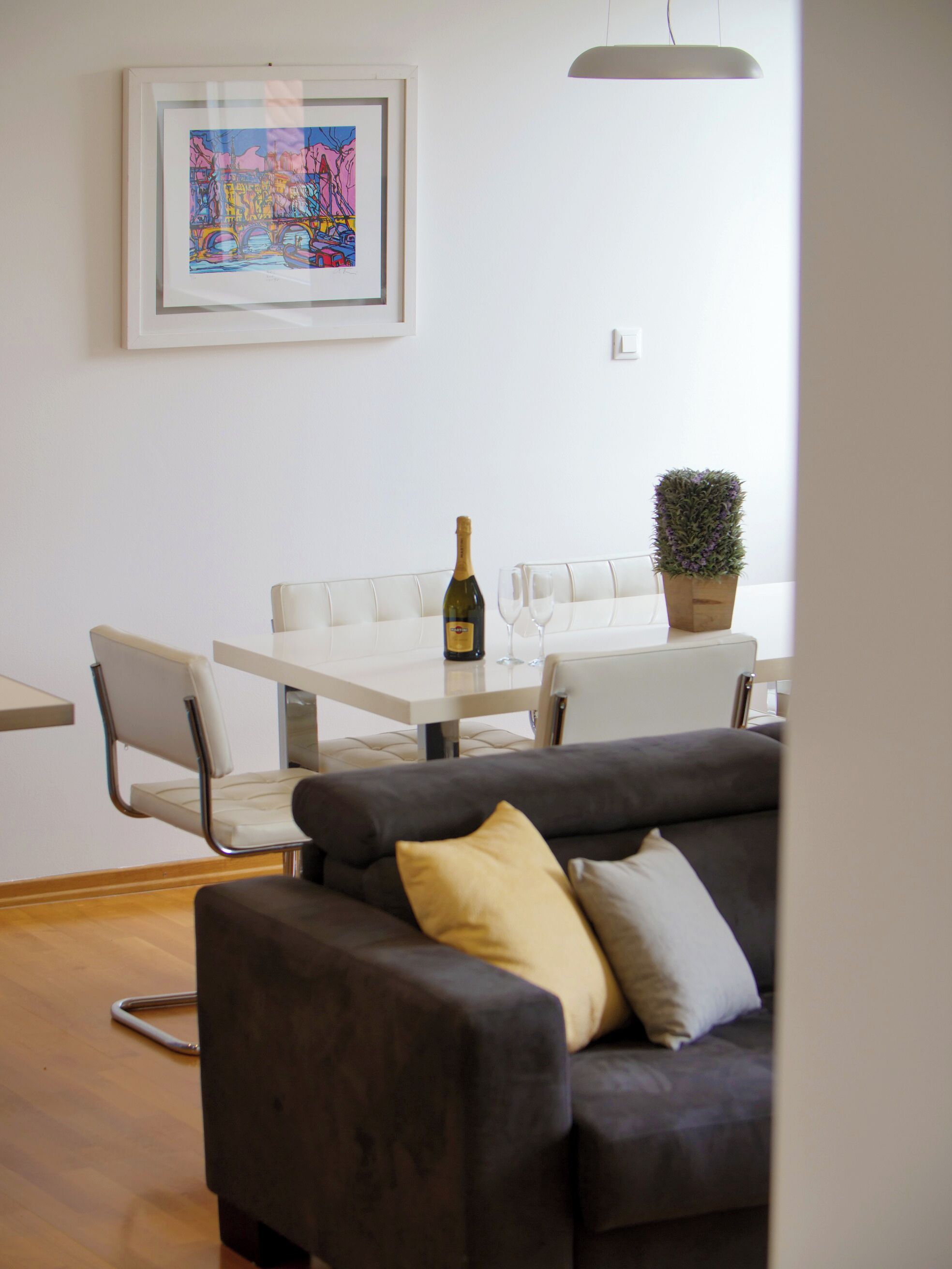 A modern living room with a gray sofa, a white dining table, and a framed artwork on the wall.