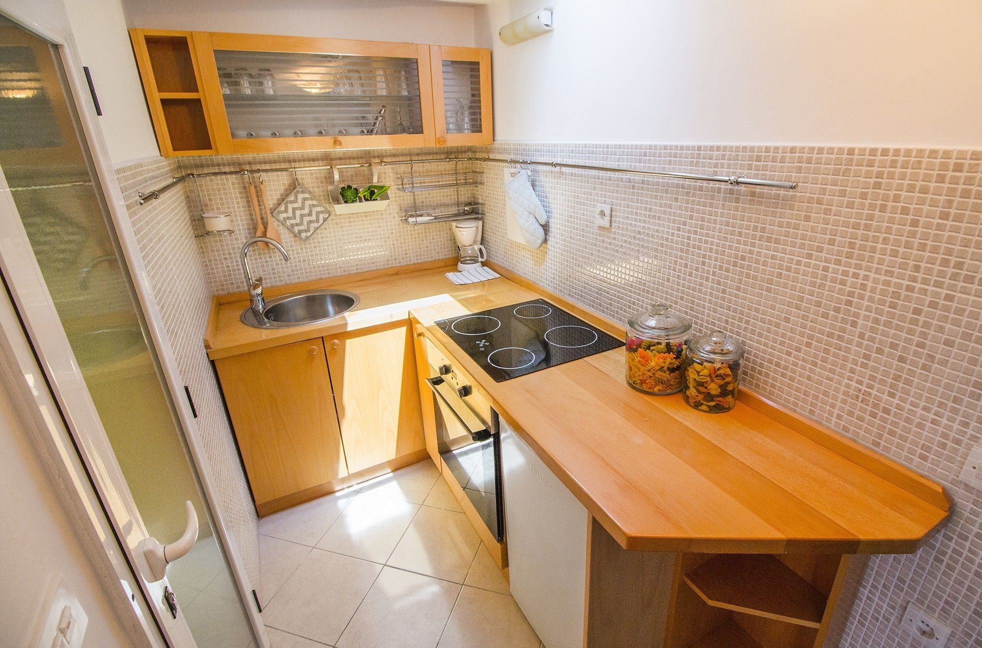 Cocina compacta con pileta, estufa y dos pequeños frascos en la encimera.