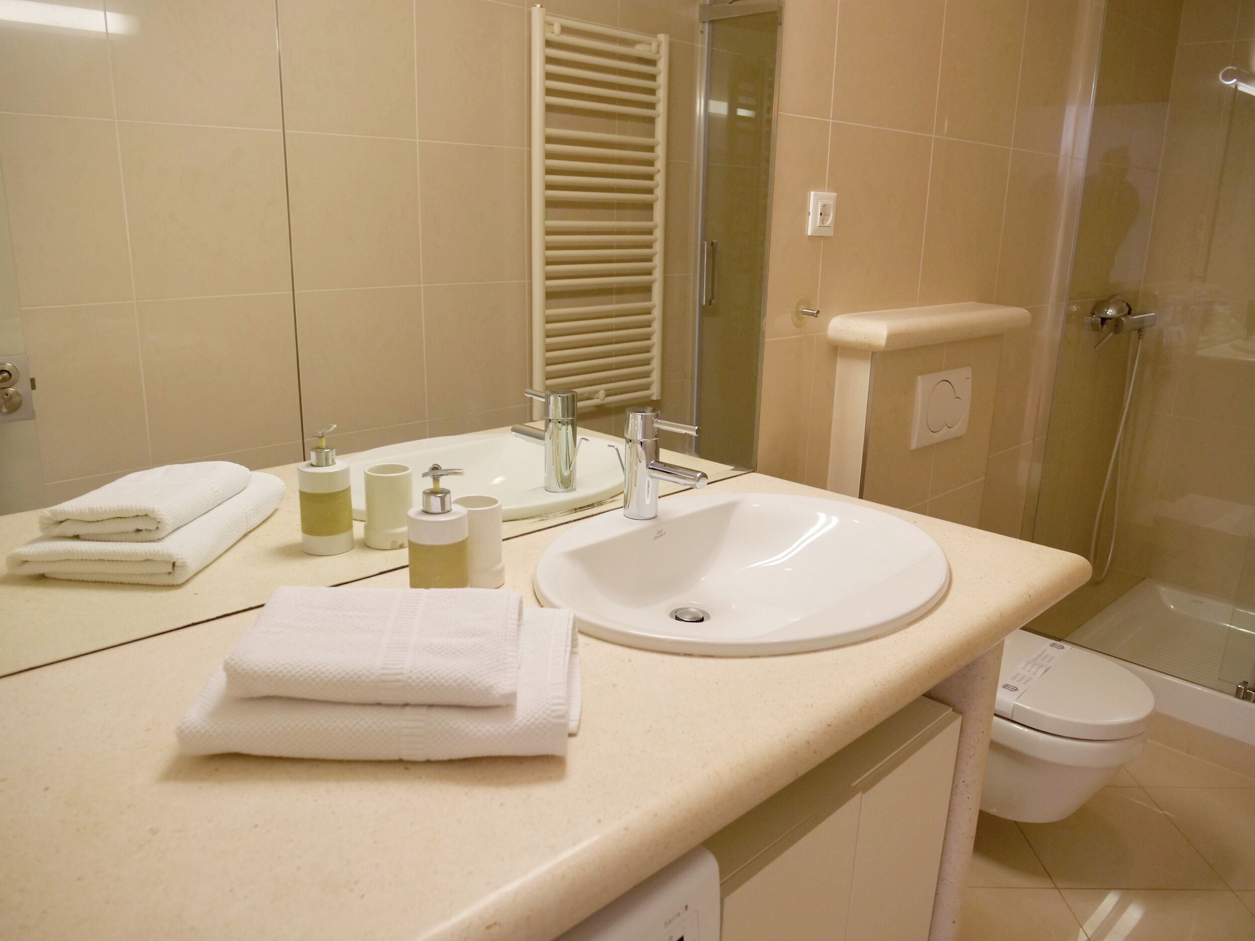 A bathroom with a sink, mirror, towel stack, and toilet.