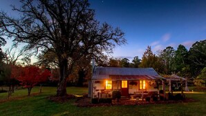A rustic cabin with a metal roof, surrounded by trees and a grassy area. - Historic Miners Cottage on Howqua River (Howqua)