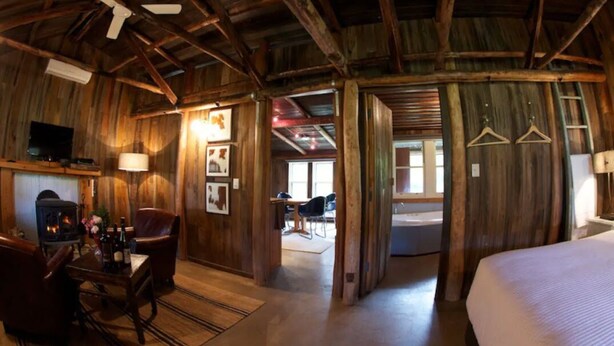 A rustic wooden room with a fireplace, a bed, and a dining area. - Historic Miners Cottage on Howqua River (Howqua)