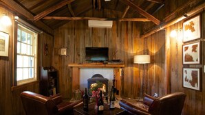 A cozy room with wooden walls, a fireplace, leather chairs, a TV, and framed pictures. - Historic Miners Cottage on Howqua River (Howqua)