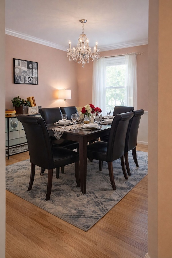 Comedor con candelabro, una mesa preparada para cuatro personas y vistas al exterior a través de un ventanal.