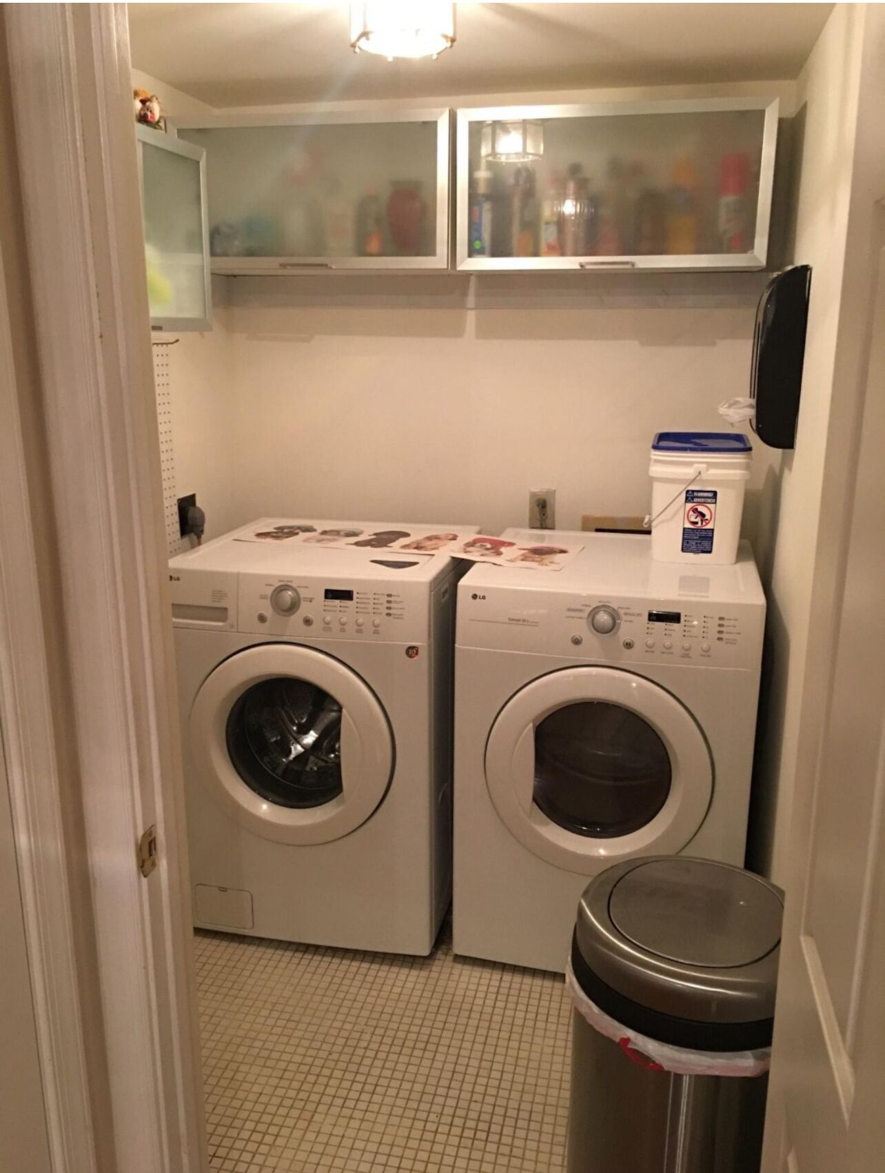 A laundry room with two front-loading washing machines and a trash can.