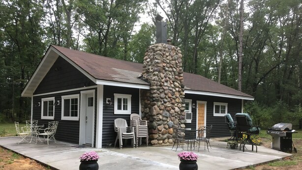 Una cabaña con chimenea de piedra, un patio con mobiliario exterior y una parrilla.