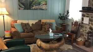 Una sala de estar acogedora con un sofá marrón, un sillón verde y una mesa de centro. Hay un cuadro en la pared, una lámpara y una pared de piedra.