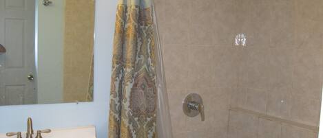 A bathroom with a sink, mirror, shower, and tiled walls.