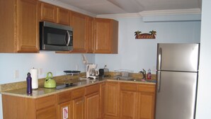 Eine Küche mit Holzausstattung, einem Edelstahlkühlschrank, einer Mikrowelle, einem Wasserkocher und einer Kaffeemaschine.
