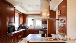 A modern kitchen with wooden cabinets, a central island with seating, and a coffee station. - SUNLIGHT VILLA WITH PRIVATE POOL  FOR FAMILIES AND FRIENDS TO ENJOY (Myrtia)