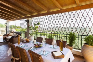 Une terrasse meublée de mobilier en osier, une table dressée pour le repas et des plantes en pot.