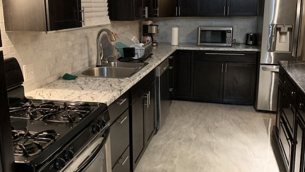 A modern kitchen with dark cabinets, stainless steel appliances, and a marble countertop. - Be At Home Away From Home II (Welland)
