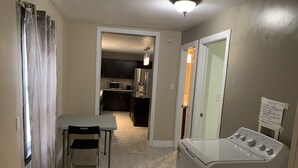 A compact kitchen with dark cabinets, a microwave, and a refrigerator. There's a dining table with a chair, and a washing machine is visible. - Be At Home Away From Home II (Welland)