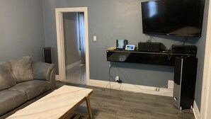 A living room with a grey couch, a wooden coffee table, a flat-screen TV mounted on the wall, and a black entertainment unit with electronic devices. - Be At Home Away From Home II (Welland)