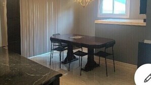 A dining area with a dark wooden table and chairs, a chandelier, a window with blinds, and a built-in shelf above the window. - Be At Home Away From Home II (Welland)