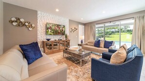Un salon avec un canapé beige, un fauteuil bleu, une table basse et un téléviseur fixé sur un mur à texture.