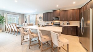 Une cuisine moderne avec des meubles en bois foncé, des appareils électroménagers en acier inoxydable et un îlot central doté de chaises.