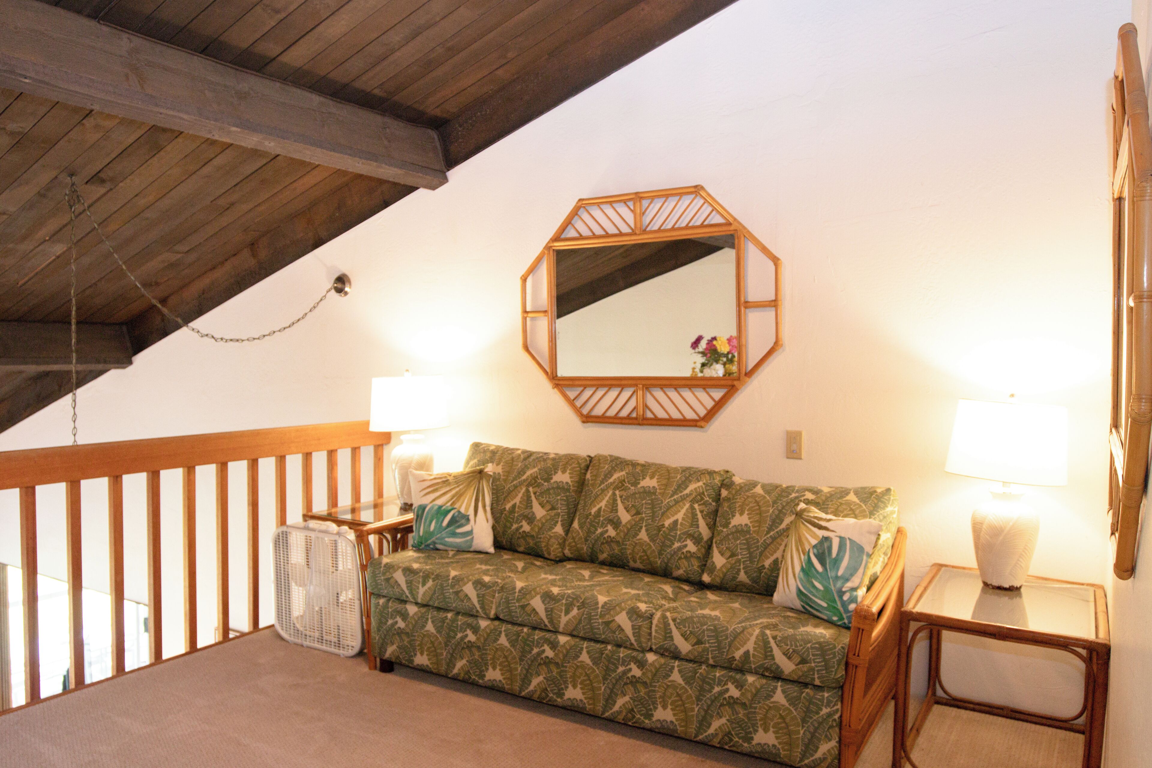 A cozy room with a wooden ceiling, a green patterned sofa, two bedside lamps, and a small table with a lamp.