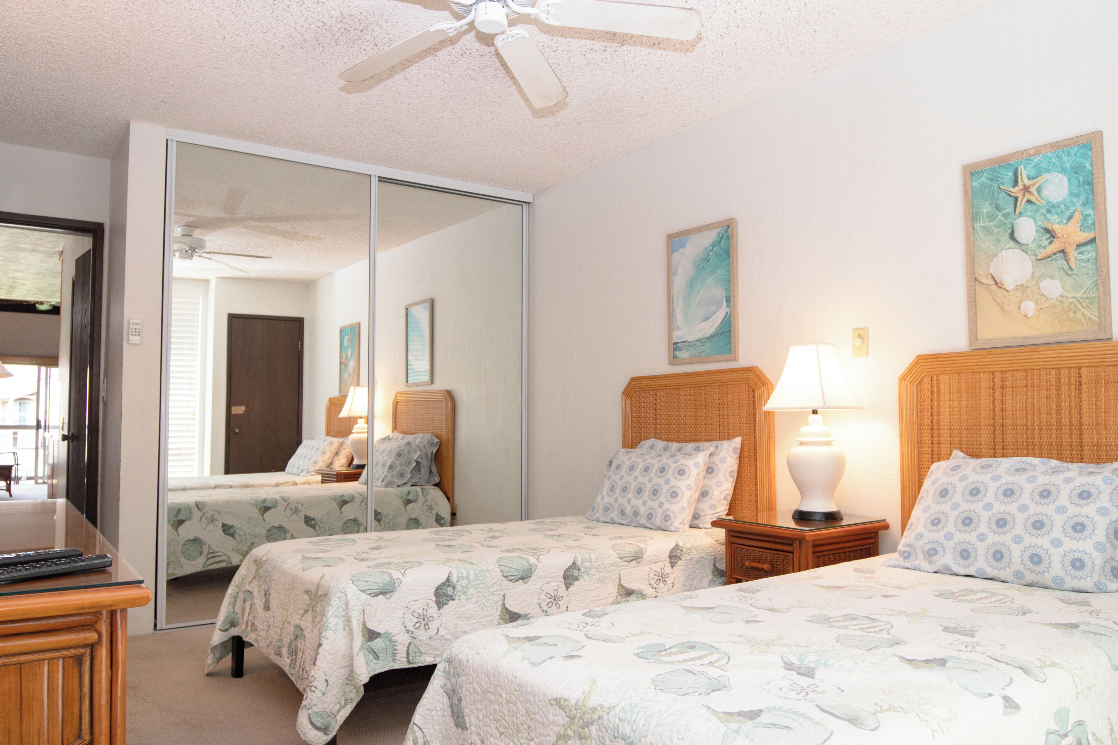 A hotel room with two beds, a ceiling fan, a mirror, and artwork on the walls.
