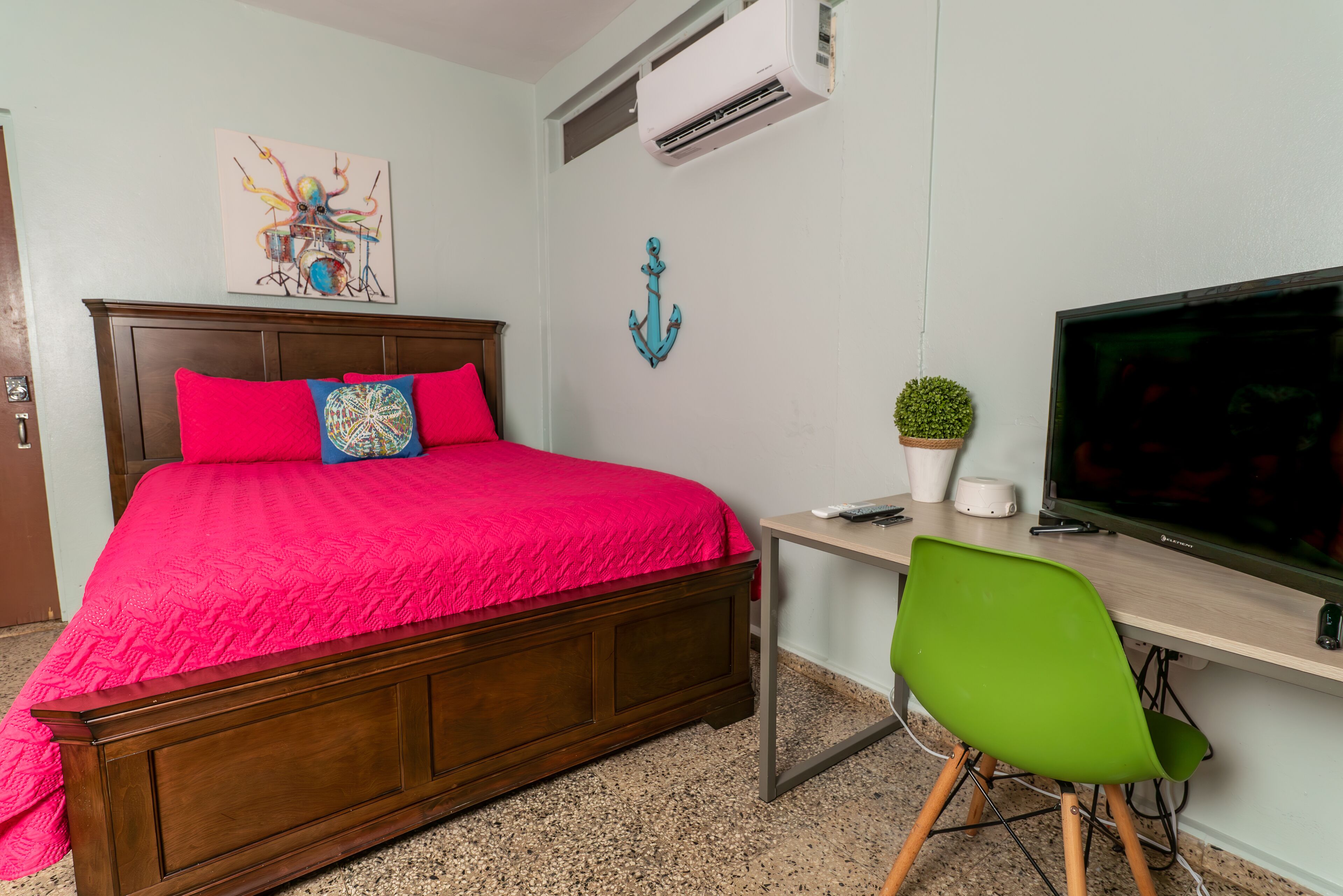 A room with a wooden bed, a desk with a computer, a TV, and a green chair.