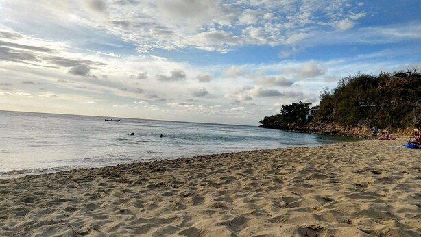 A beach with sand, water, and a distant shoreline with vegetation and buildings.