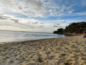 A beach with sand, water, and a distant shoreline with vegetation and buildings.