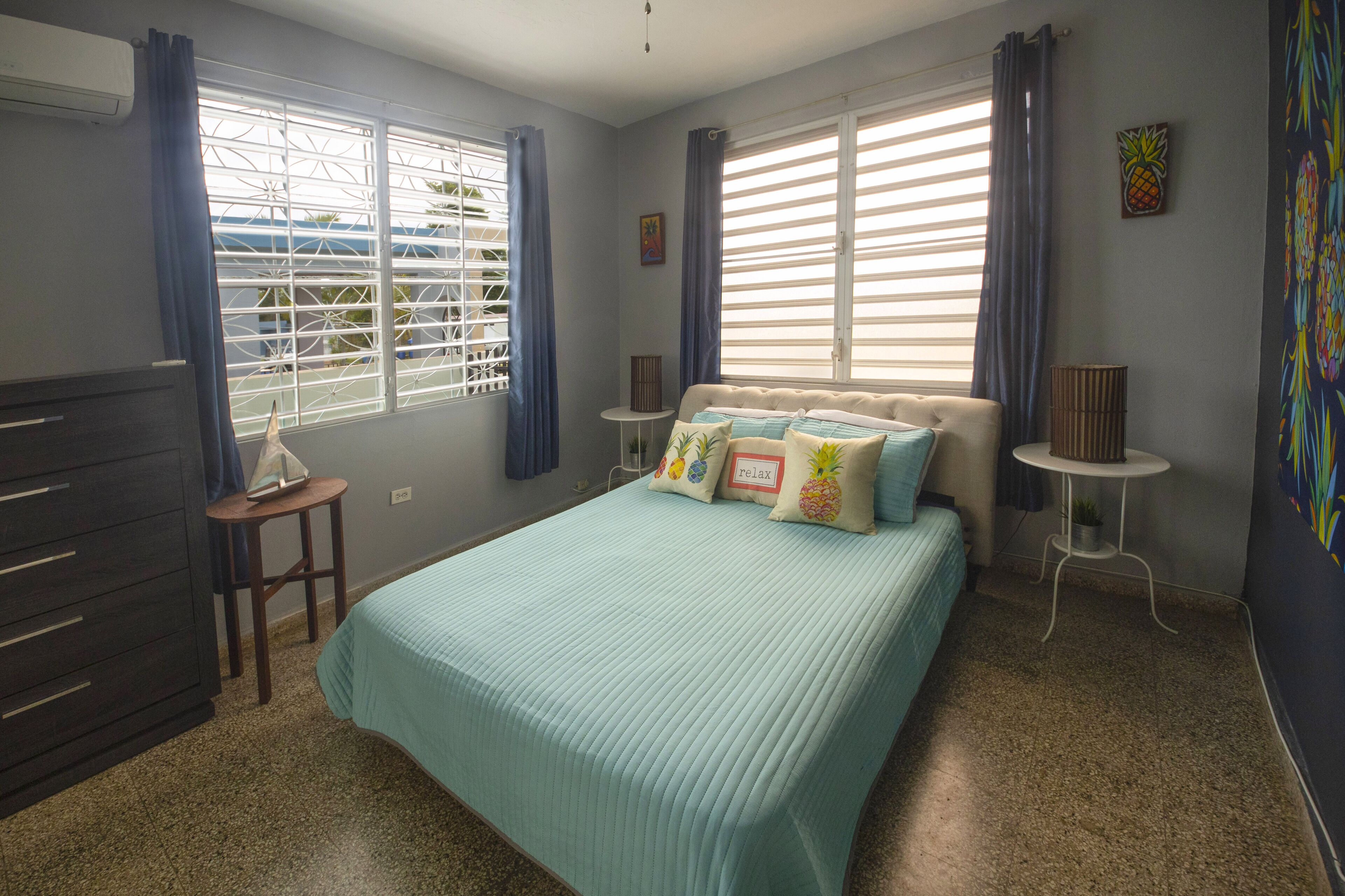 A bedroom with a bed, a dresser, a small table, and a window with curtains.