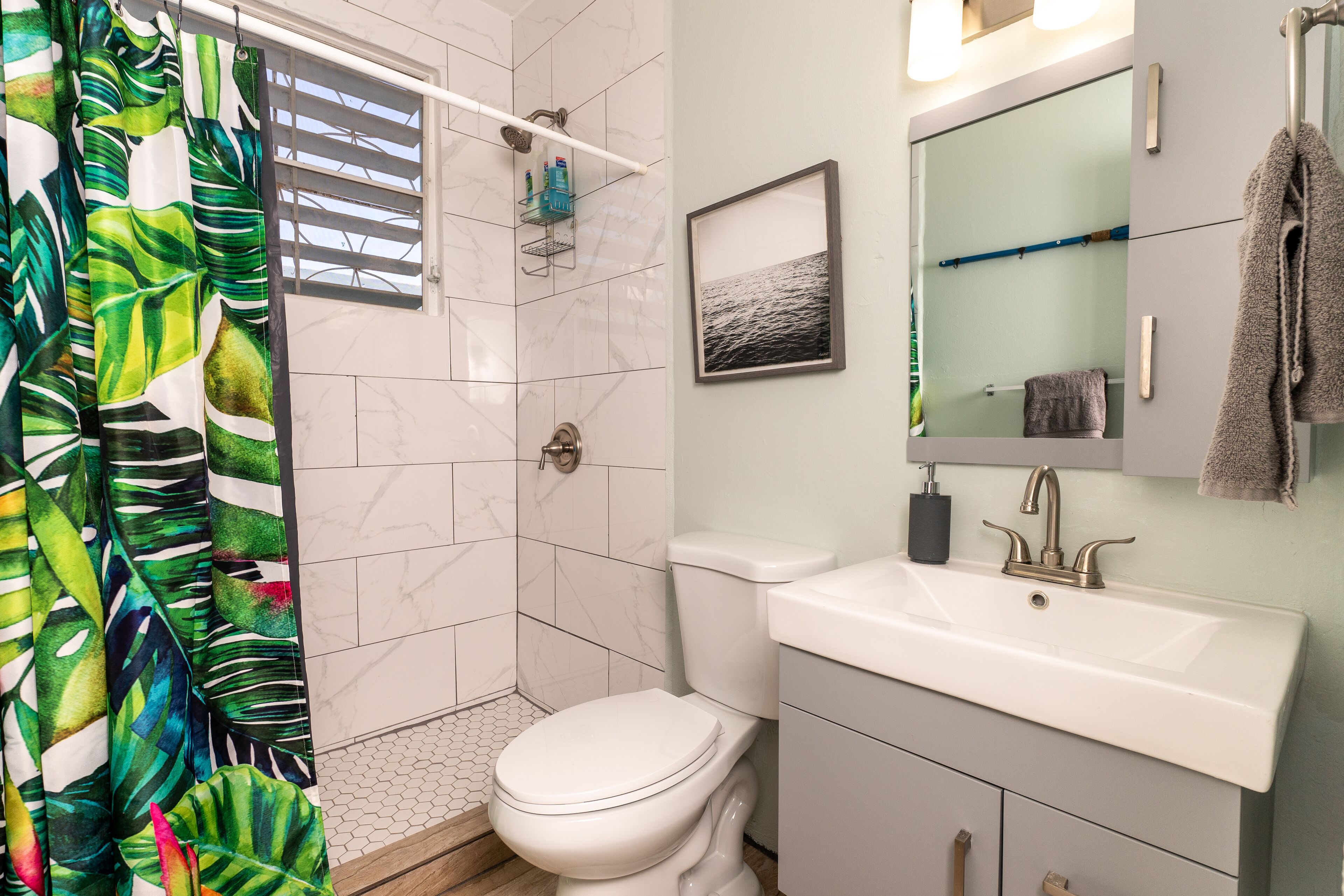 A bathroom with a shower, toilet, sink, and a framed picture on the wall.