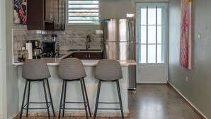 A kitchen with a ceiling fan, a refrigerator, a coffee maker, and a window with blinds.