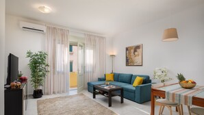 A modern living room with a sofa, coffee table, TV, and a dining area with a table and chairs. - Sun Spalato City (Split)