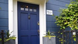 Une porte bleue avec une plaque indiquant « Catamount House, construite en 1922 », et deux plantes en pot de chaque côté.