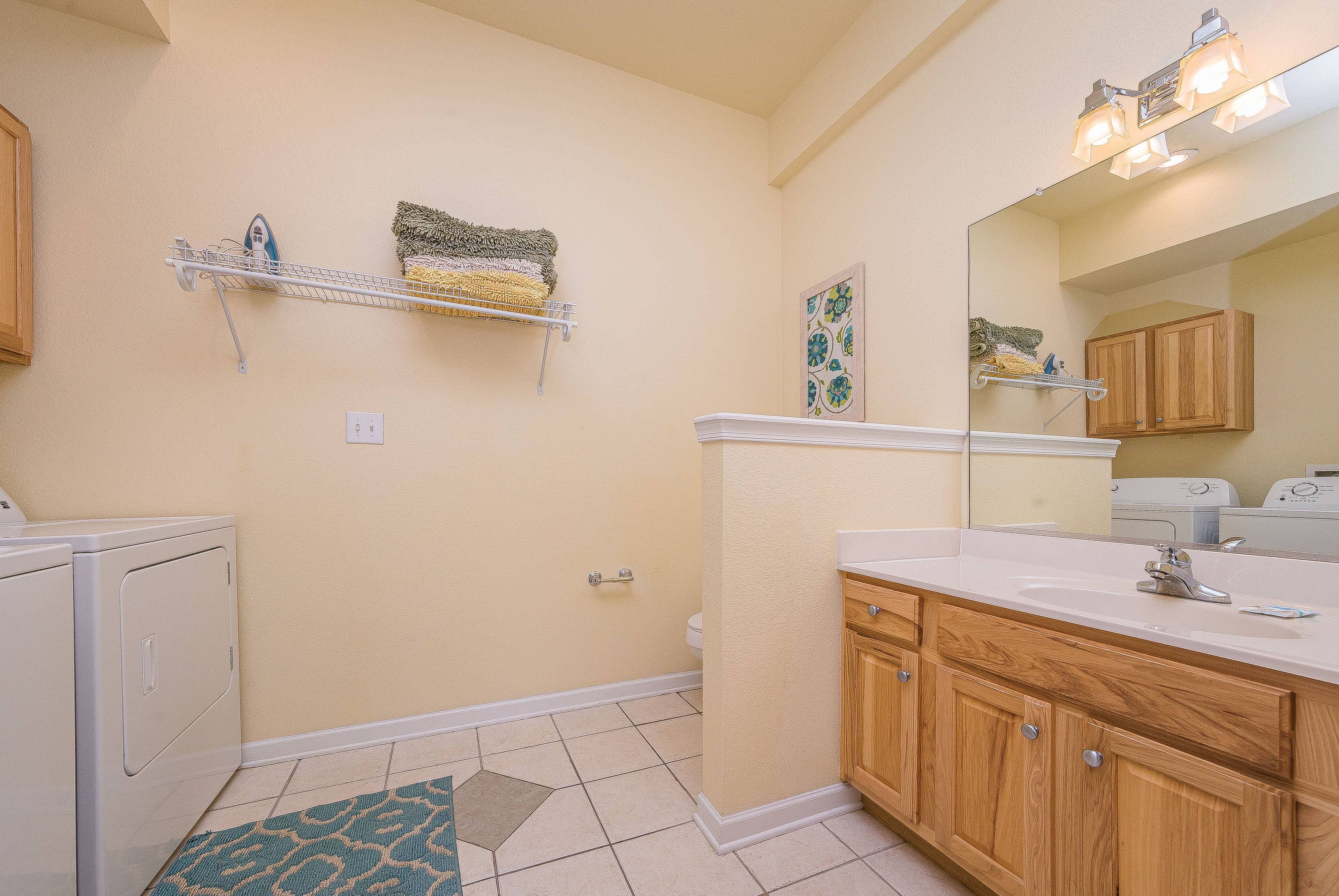 A bathroom with a white sink, wooden vanity, a mirror, a towel rack, and a laundry machine.