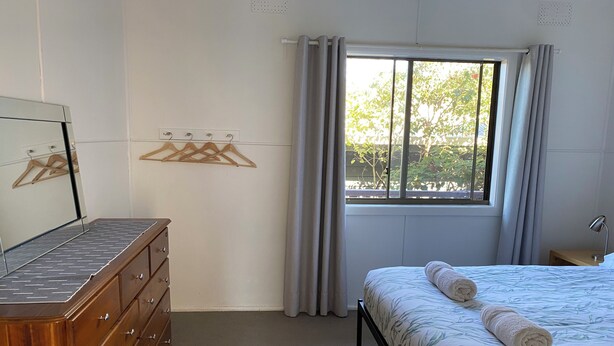A bedroom with a bed, a dresser, a window with curtains, and a mirror. - Unit 3 Beachside units.  Pambula Beach (Pambula Beach)