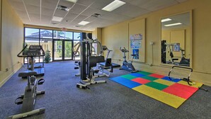 Ein Fitnessraum mit unterschiedlichen Trainingsgeräten, einer bunten Matte und großen Fenstern.