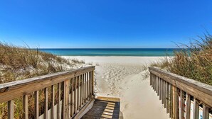 Ein hölzerner Steg führt zu einem Sandstrand mit klarem, blauem Wasser.