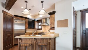 A kitchen with wooden cabinets, a stainless steel refrigerator, a large island with stools, and pendant lighting.