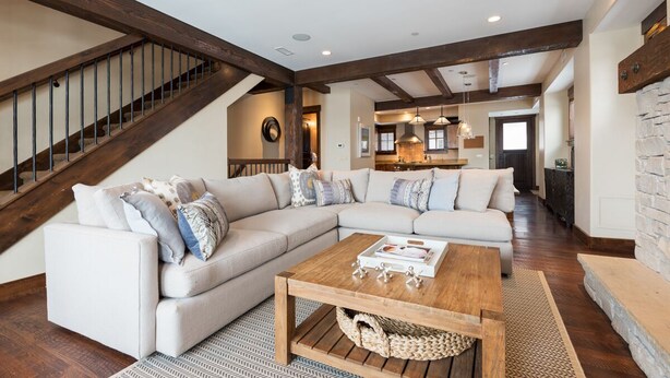 A spacious living room with a large sectional sofa, a wooden coffee table, and a staircase with exposed beams.