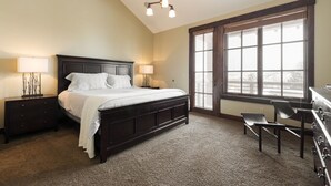 A bedroom with a large bed, two bedside tables with lamps, a dresser, and a window with blinds.