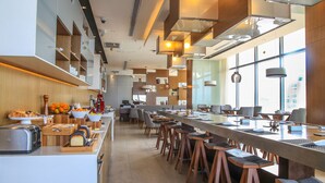 Une cuisine d’hôtel moderne, dotée d’un long comptoir, de tabourets de bar et d’un assortiment de produits pour le petit-déjeuner.