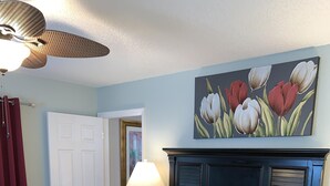 Un lit bien fait, recouvert d’une couvre-lit à motifs, une tête de lit ornée d’un tableau de fleurs, une lampe de chevet et un tapis rouge.